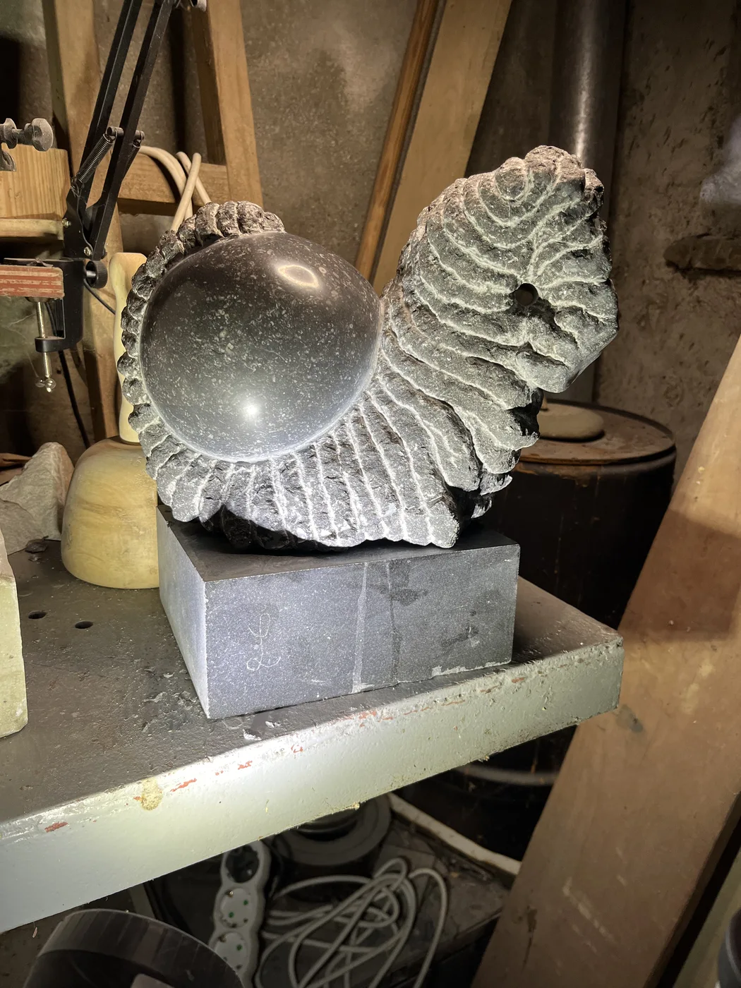 Black marble Shamir II on the workbench, with pale carved edges and a smooth dark centre